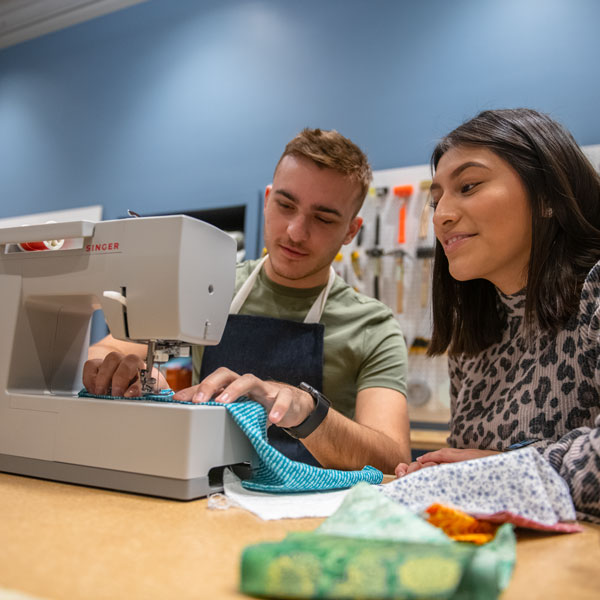 Two students work on a sewing machine.